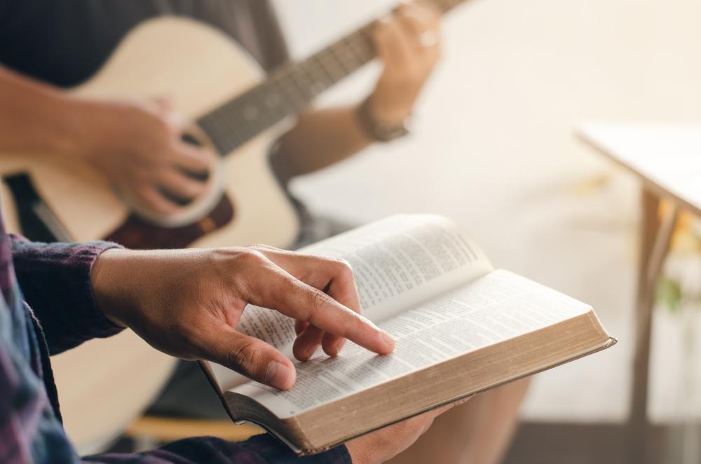 Sormi osoittaa tekstiä raamatun lehdellä, taustalla kitara ja kitaristi.