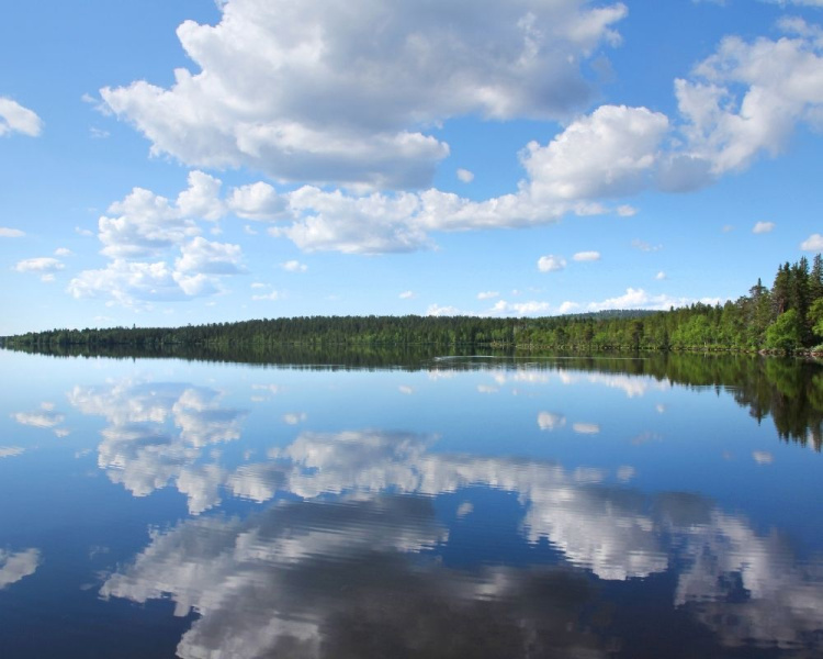 Kesäinen järvimaisema, tyyni vesi ja valkoisten pilvien heijastus veden pintaan.