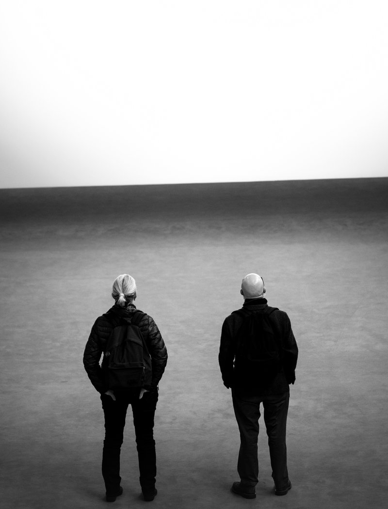 Mies ja nainen seisovat rannalla ja katselevat aavalle merelle selin kuvaajaan päin.