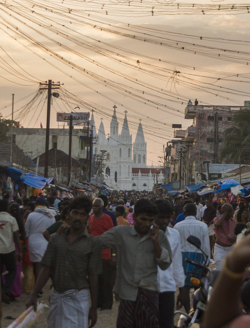 Intialaisella kadulla kulkee paljon ihmisiä. Taustalla kirkko.