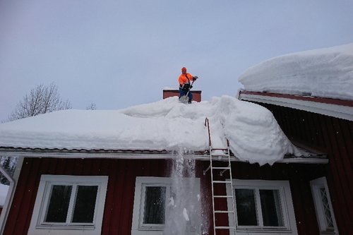 Mies pudottaa lunta katolta.